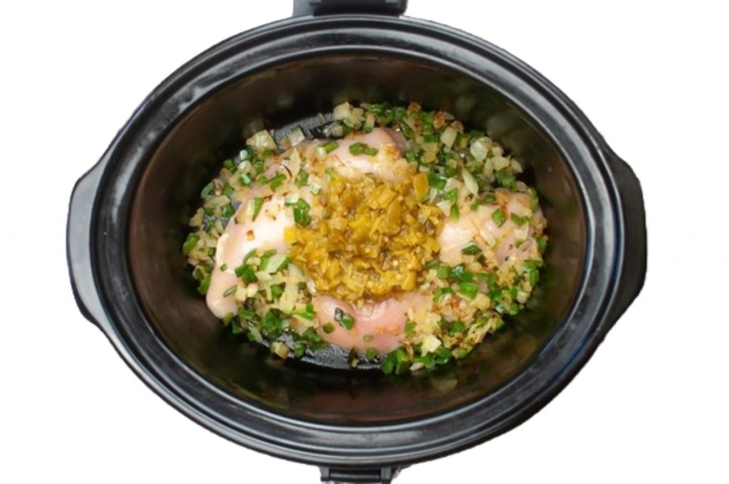 A top view of a crockpot with chicken ready to be cooked. 