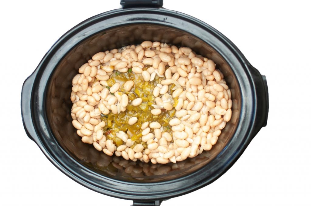 A top view of a crockpot filled with white beans and green chilis.