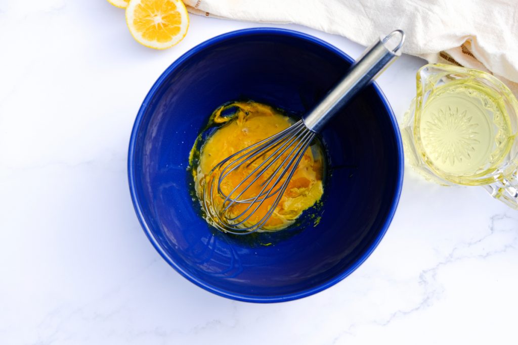 A blue mixing bowl with egg yolks and a metal whisk. 