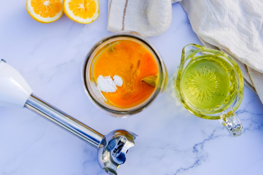 An immersion blender next to a mason jar with eggs and oil on the side. 