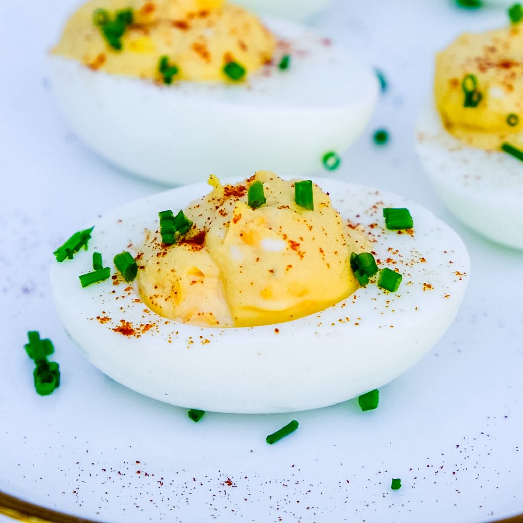 Deviled egg topped with chives and paprika on a white plater