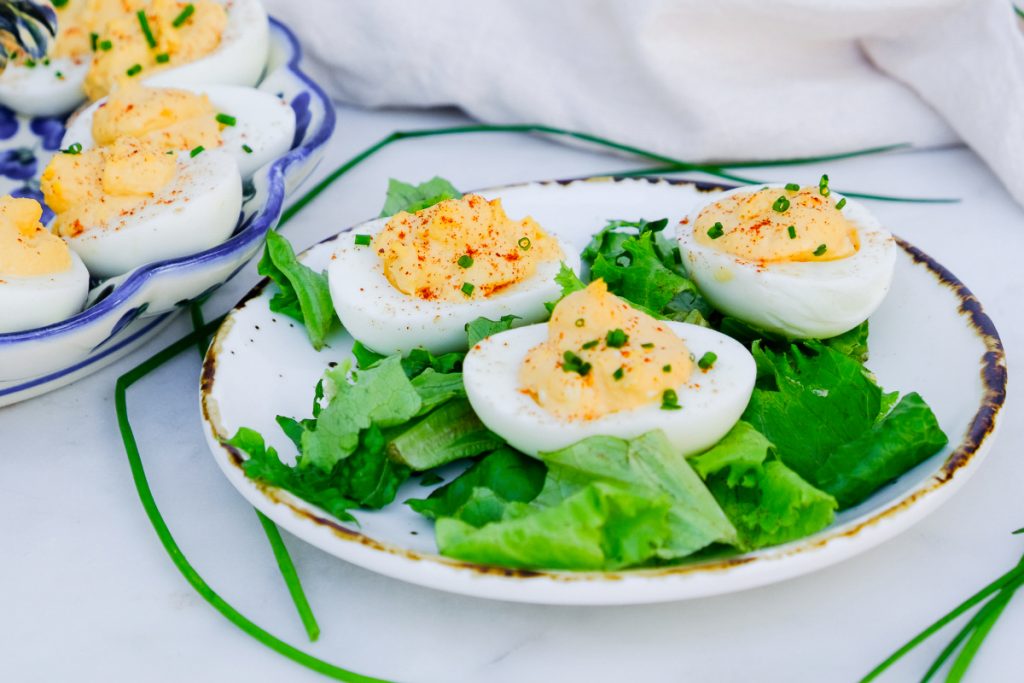 Cooked egg whites sliced and filled with yolk mixture on a white plate with green lettuce. 