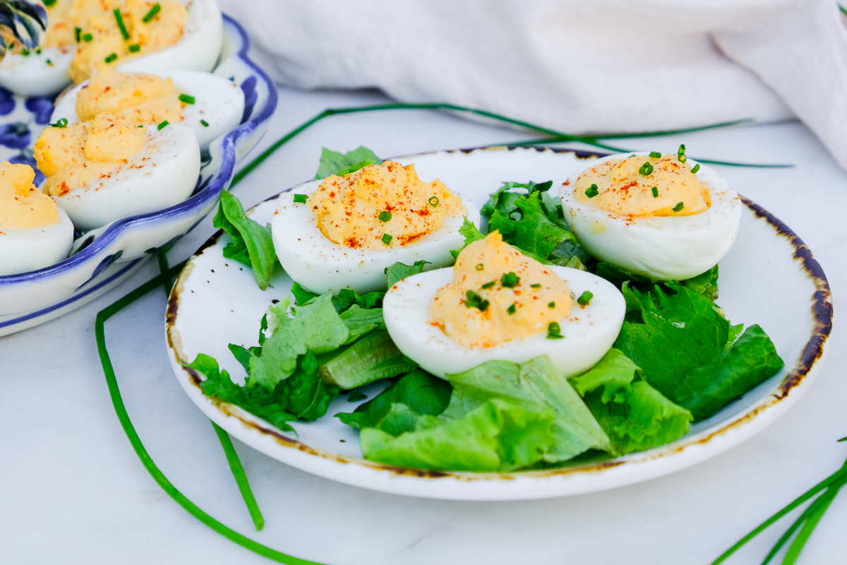 Cooked egg whites sliced and filled with yolk mixture on a white plate with green lettuce.