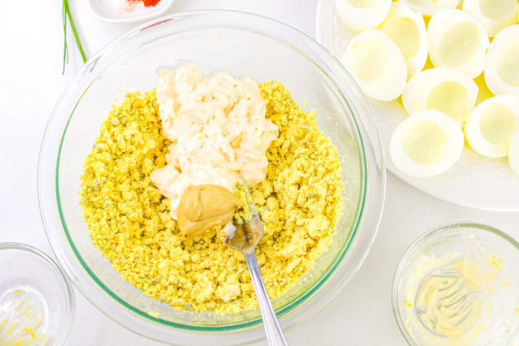 Egg yolks in a clear mixing bowl with mayonnaise and dijon mustard.