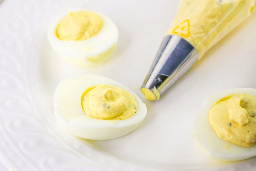 A piping bag filled with deviled egg mixture filling half of a cooked egg white.