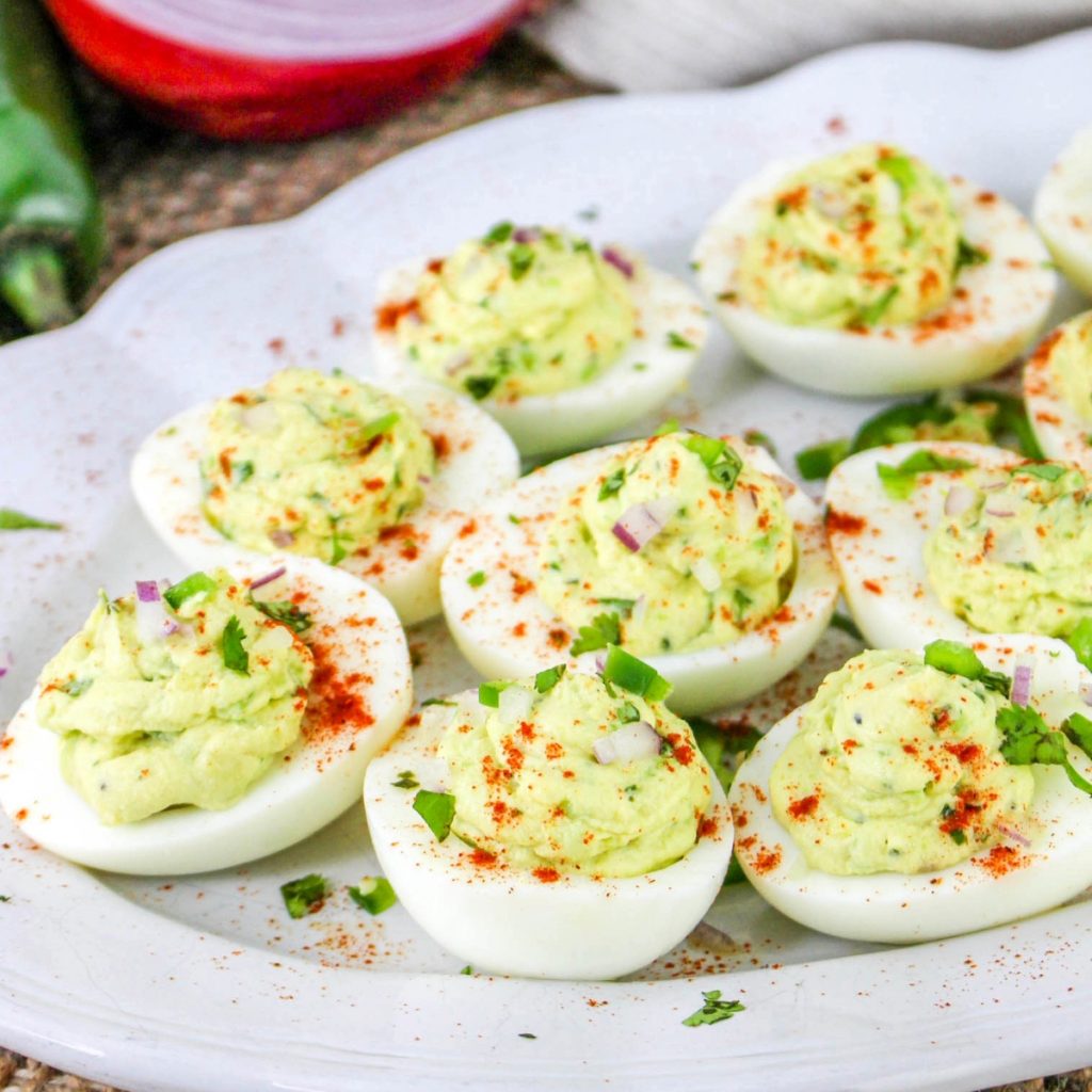 Spicy avocado deviled eggs on a white plate sprinkled with paprika.