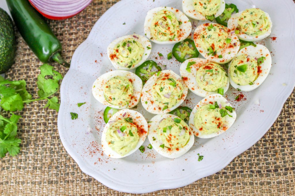 Stuffed deviled eggs on a white serving platter with jalapenos on the side. 