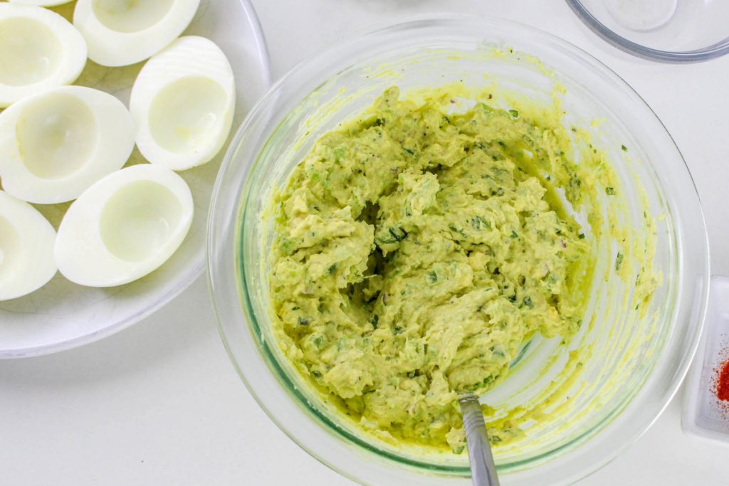 Cooked half egg whites on a serving dish with deviled egg mix in a mixing bowl on the side. 