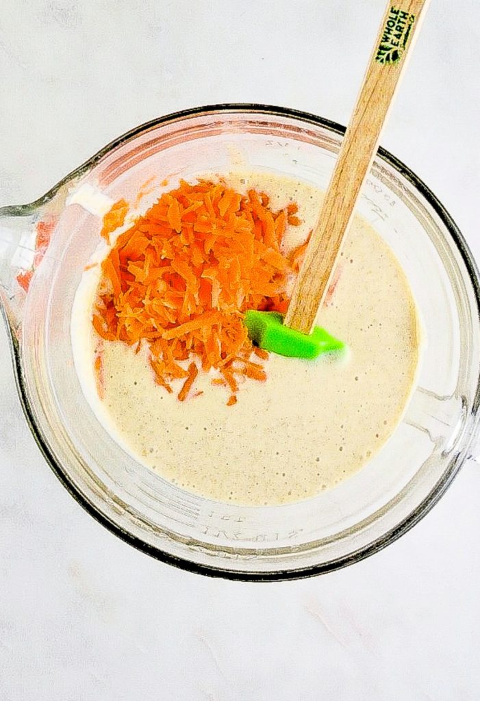 Shredded carrots folded into cake batter in a clear mixing bowl. 