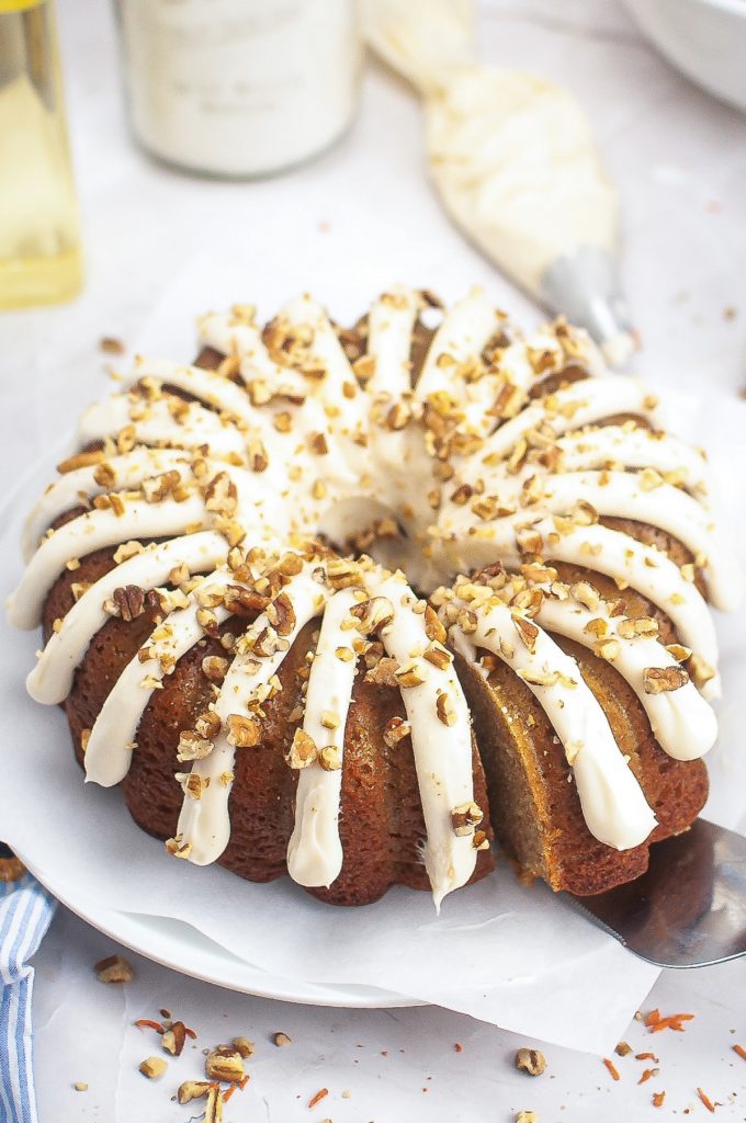 Bundt cake with cream cheese frosting on a white serving plate. 