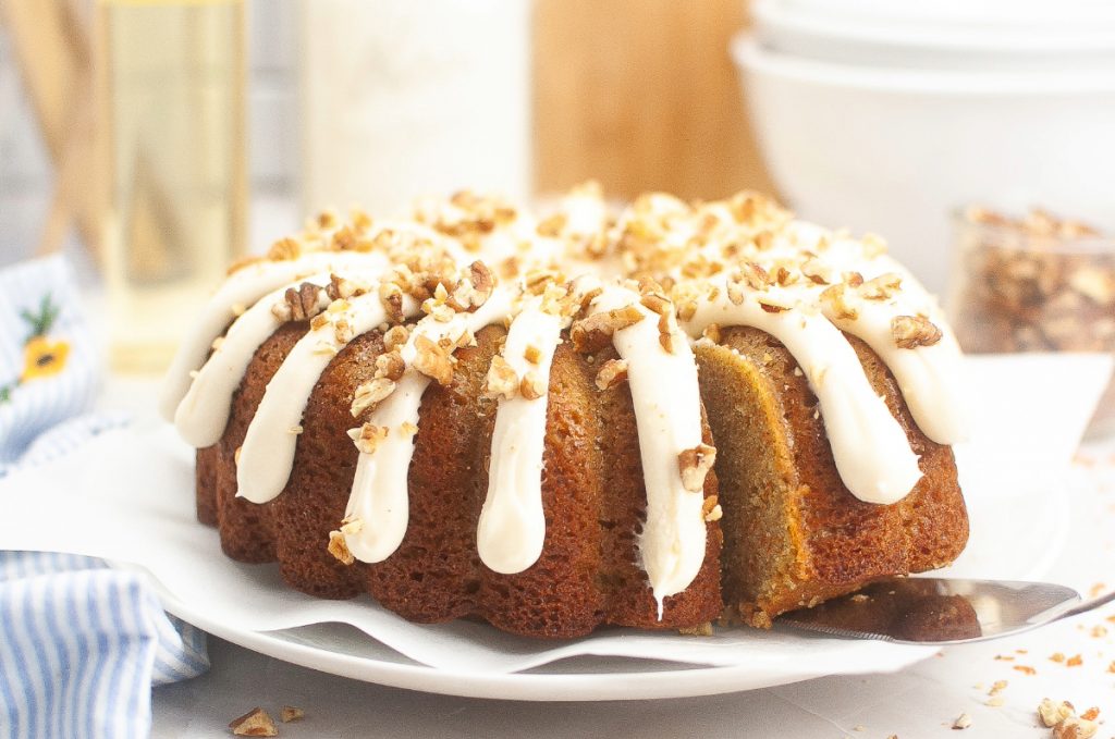 A whole cake on a white serving platter topped with cream cheese frosting. 