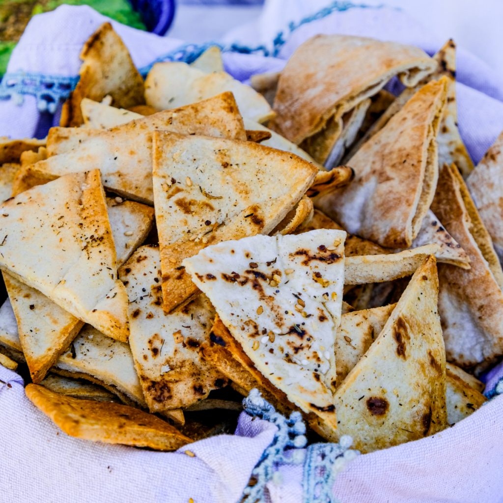 Pita chips in a basket lined with a tan fabric napkin.