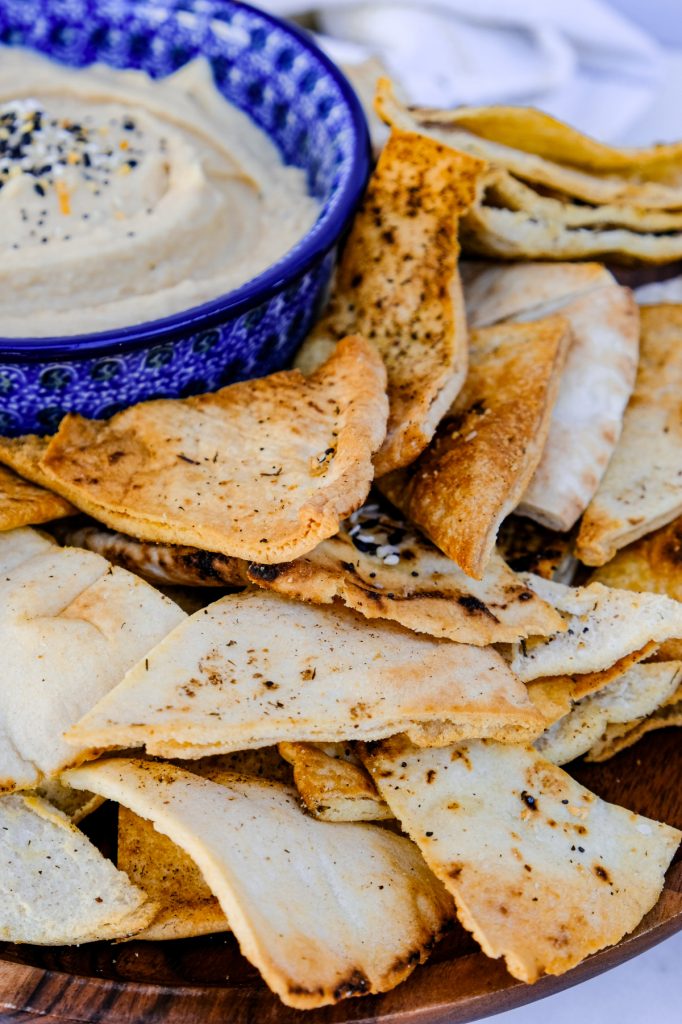 Homemade pita chips on a platter with hummus on the side for dipping. 