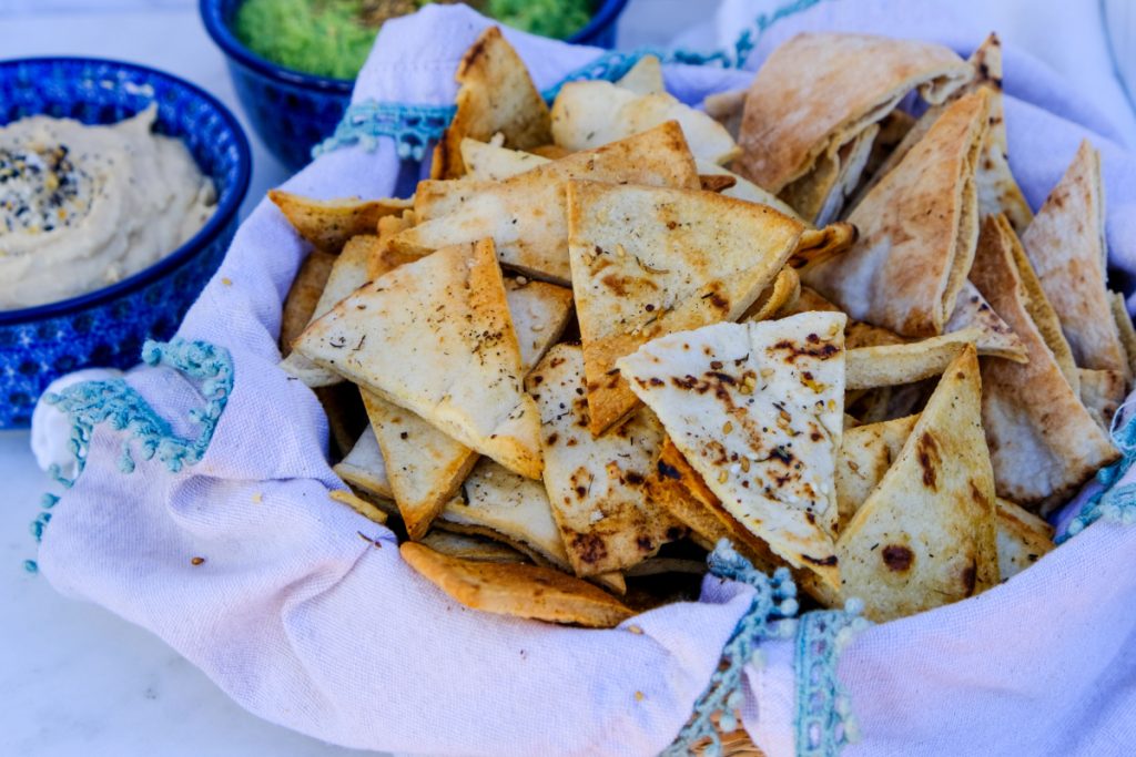 A bowl filled with air fryer pita chips with a bowl of hummus on the side. 