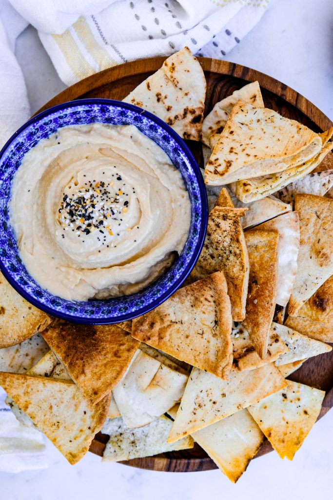 Overhead view of a brown serving dish with air fryer pita chips with a bowl of hummus on the side. 