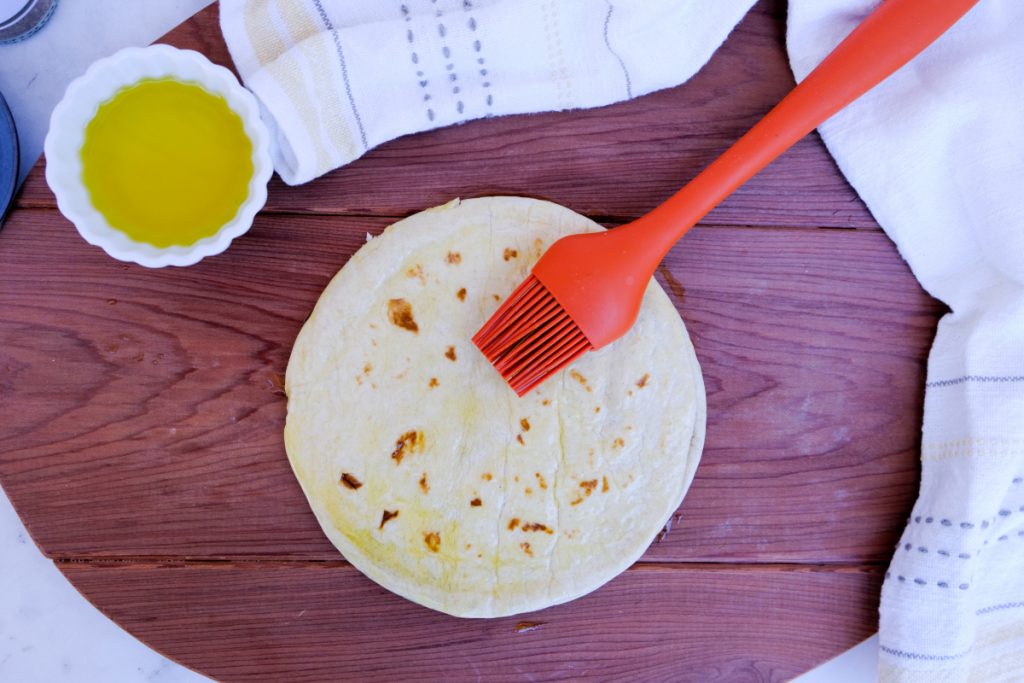 Pita bread on a brown cutting board with a pastry brush adding oil.