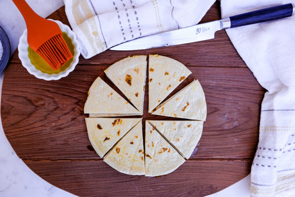Pita bread on a brown cutting board cut into triangles.