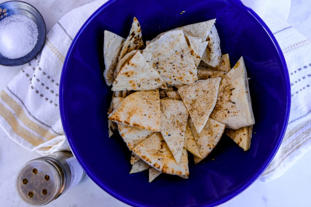 Sliced pita triangles in a blue mixing bowl seasoned with salt. 