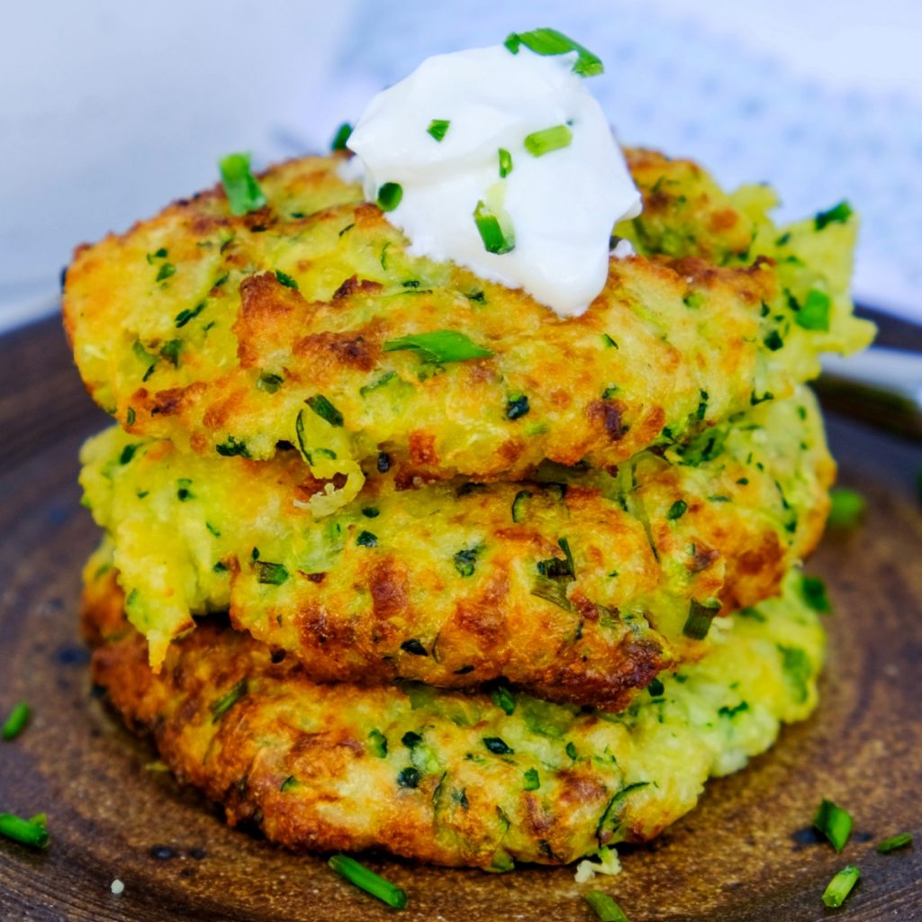 A stack of air fryer zucchini fritters topped with sour cream and chives.