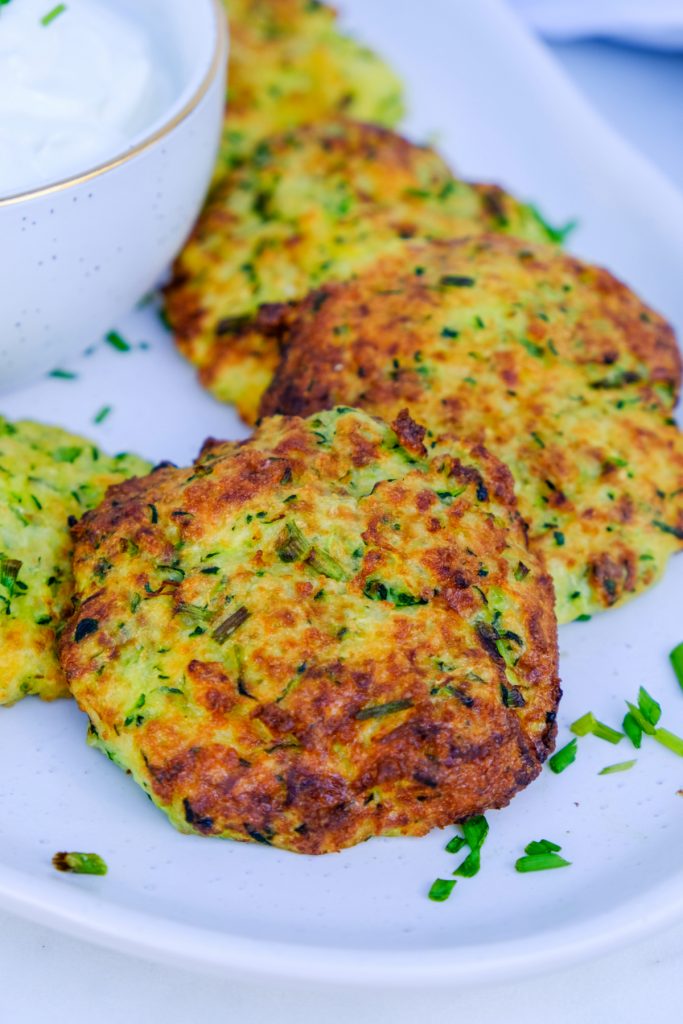 Healthy zucchini fritters air fried on a white serving dish topped with chopped chives. 