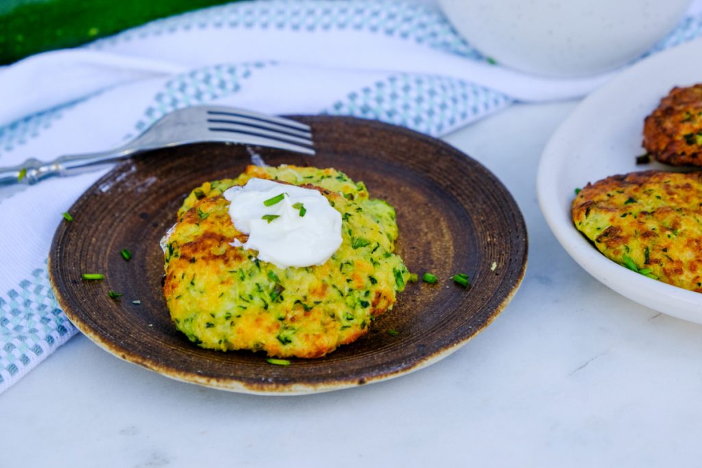 Air fryer zucchini fritters on a brown dish topped with sour cream ready to eat.