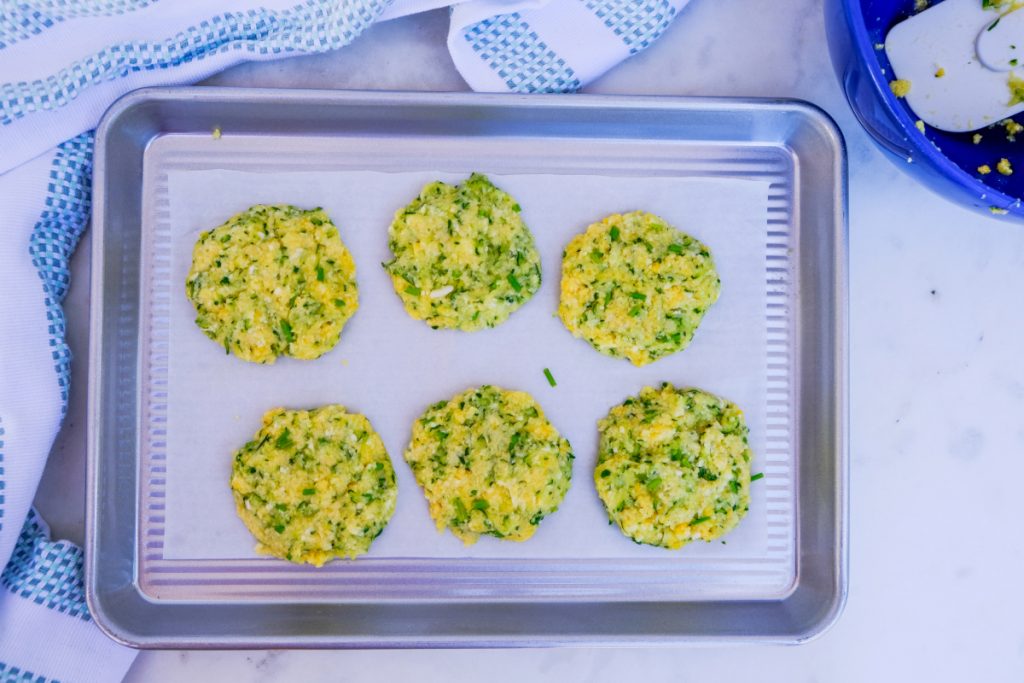 Shaped zucchini fritters placed on a parchment lined baking sheet. 