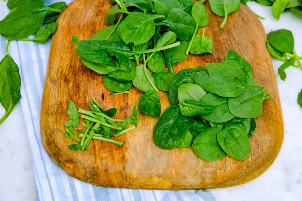 Baby spinach on a cutting board with the stems removed. 