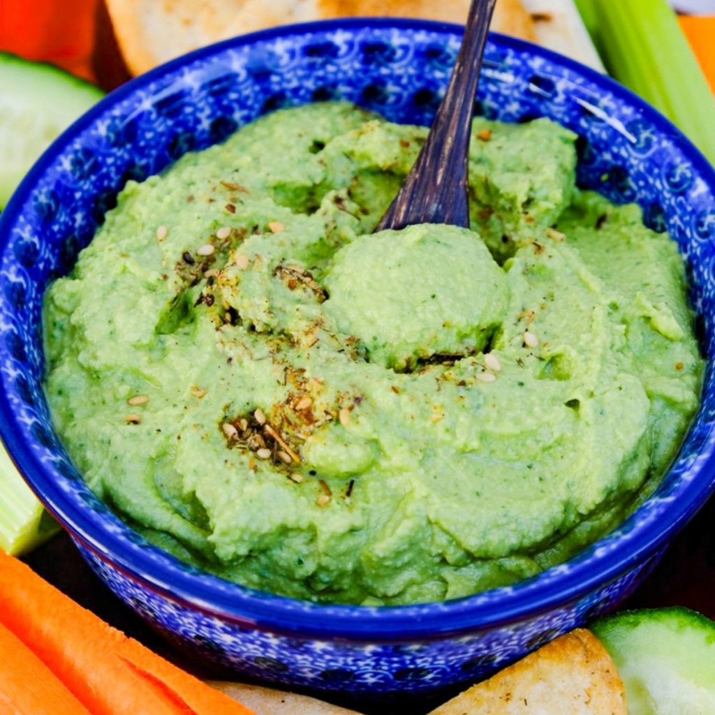 Homemade spinach hummus in a blue serving bowl surrounded with vegetables.