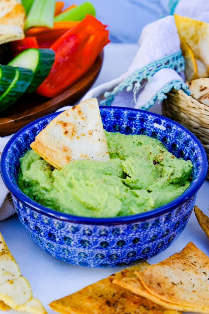 Hummus in a small bowl with vegetables and pita chips on the side. 