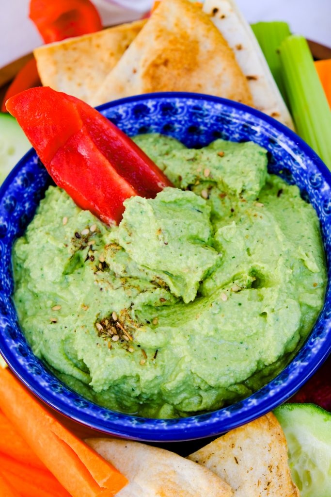An overhead view of spinach hummus with a slice of red bell pepper dipping in getting a scoop. 