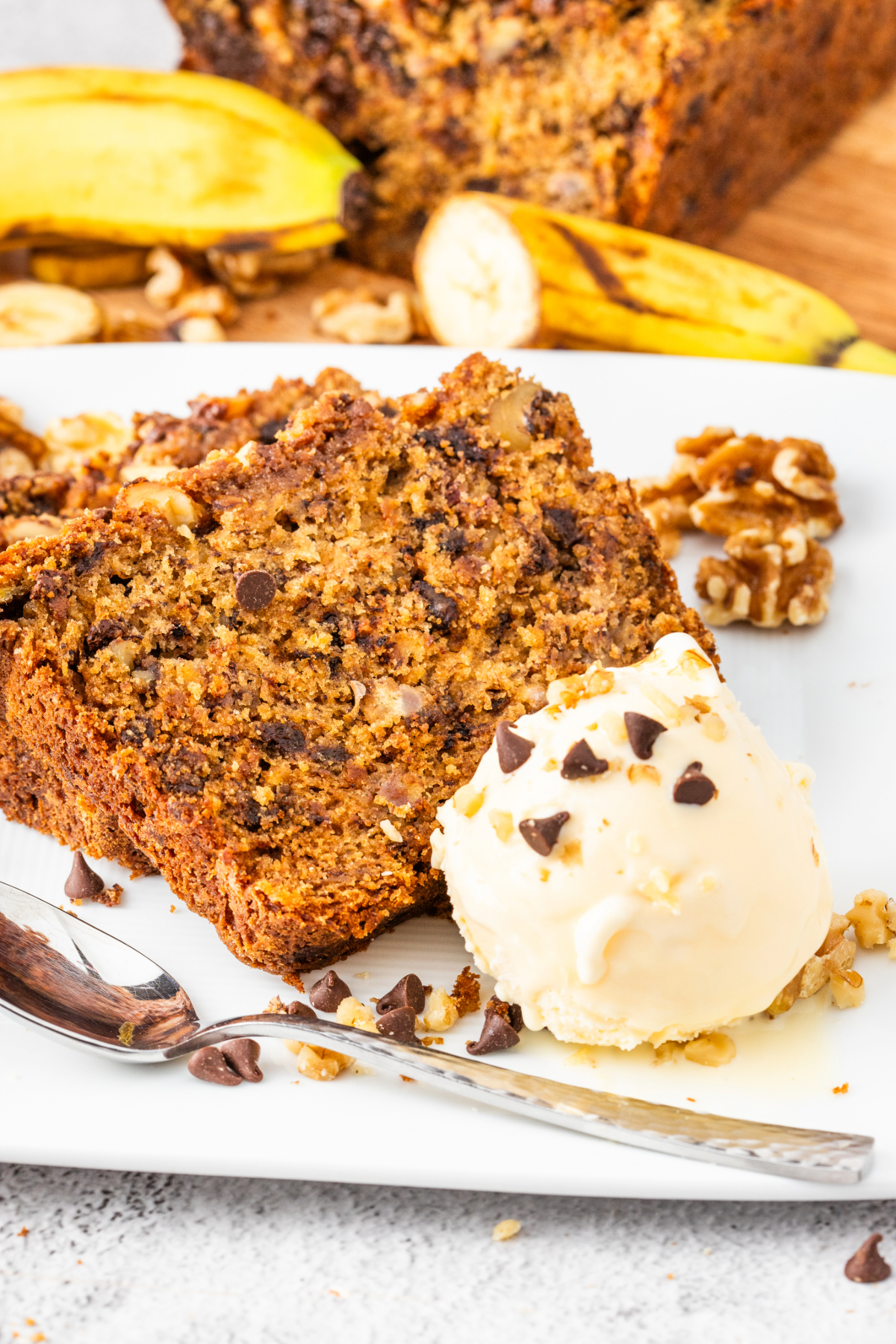 Sliced banana bread with a scoop of vanilla ice cream on a white plate. 