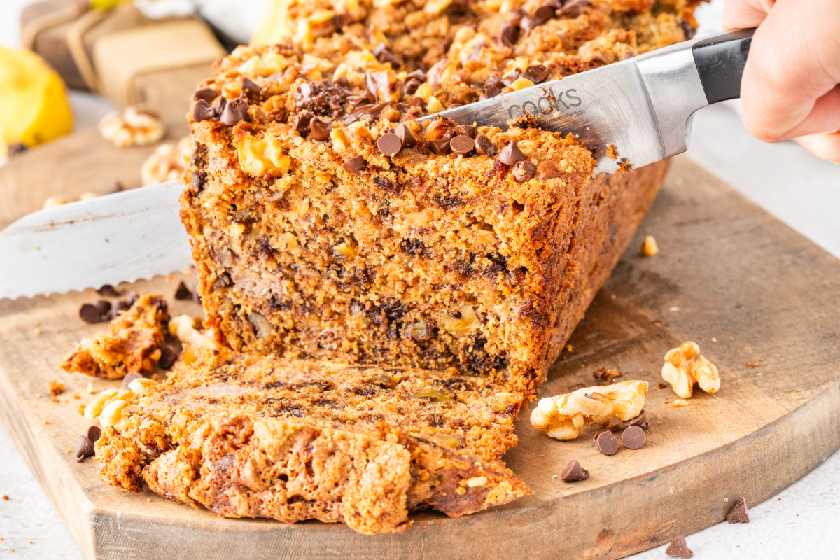 With a knife slicing banana bread on a wooden cutting board.