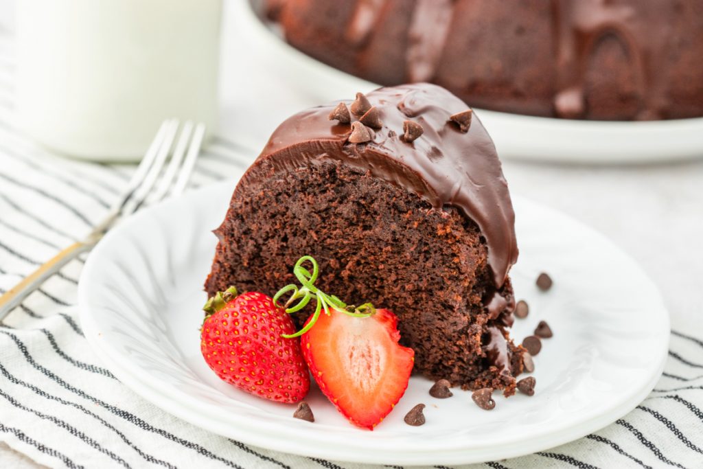 A slice of cake on a white plate with sliced strawberry on the side. 