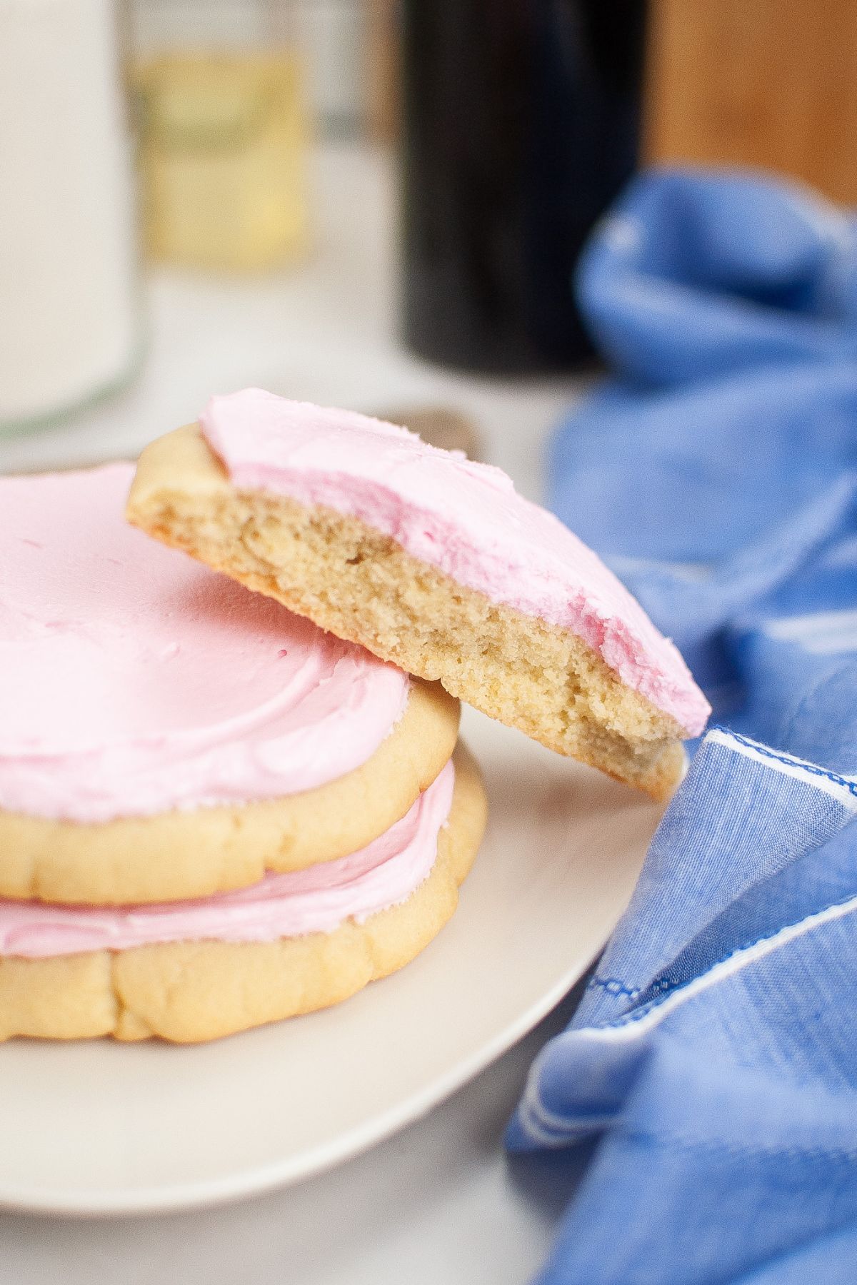 Three pink sugar cookies stacked on a plate with one of them biten in half.