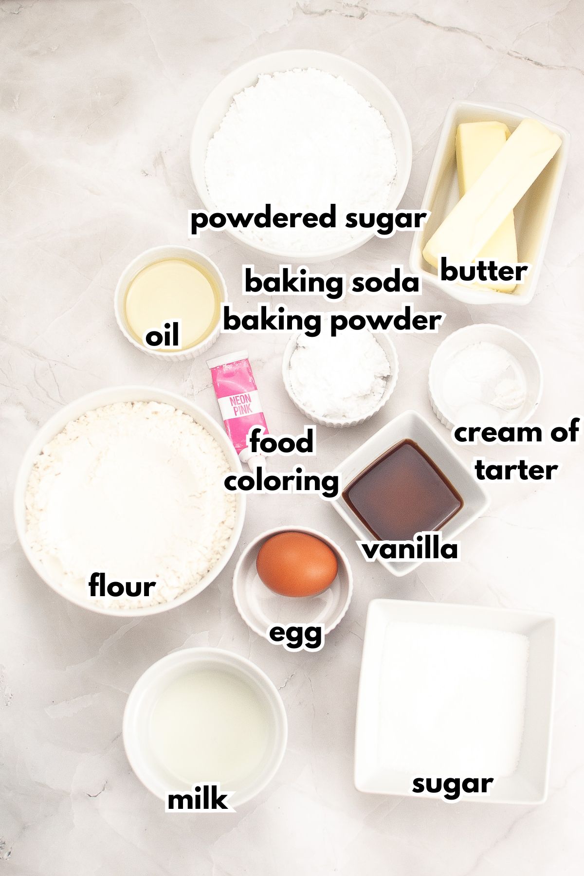Bowls of powdered sugar, oil, baking soda and powder, butter, food coloring, flour, egg, vanilla, cream of tatter, milk, and sugar on a counter.