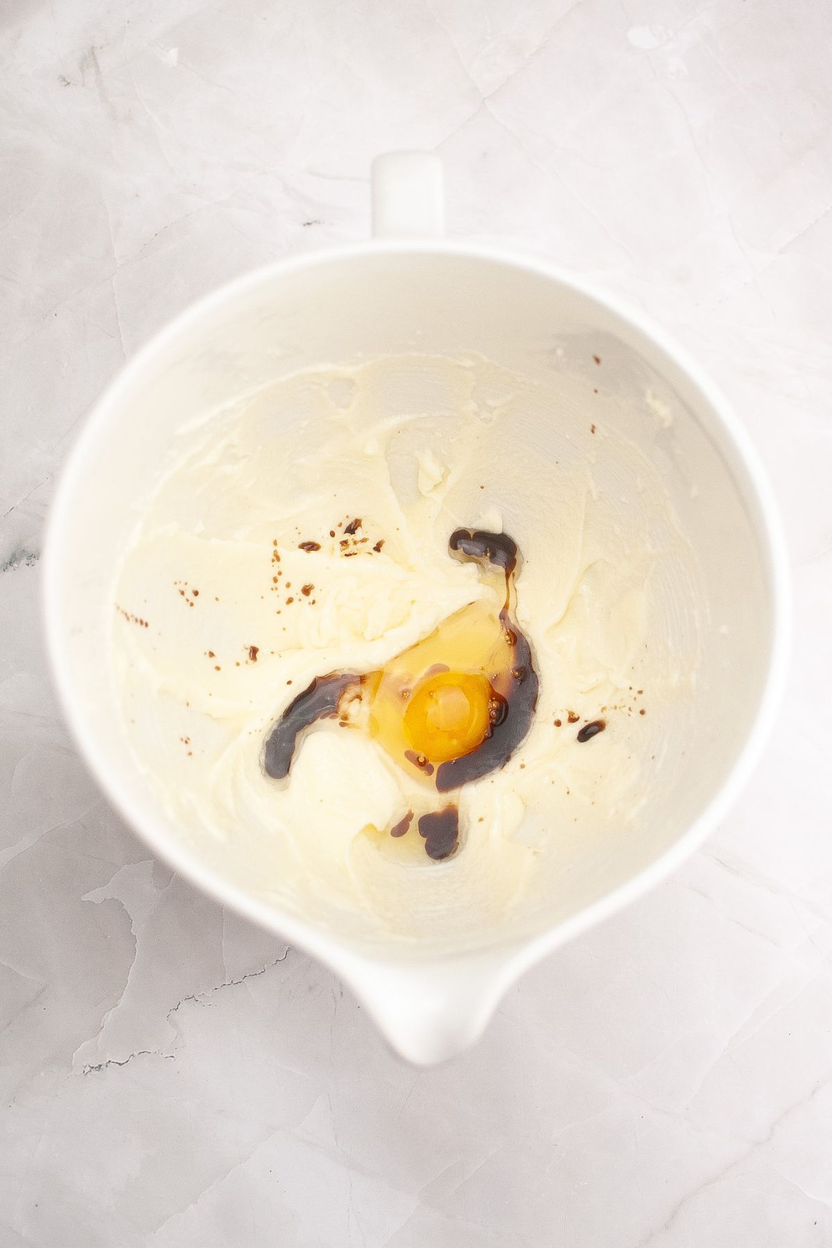 Eggs and vanilla being added to butter and sugar in a large mixing bowl.