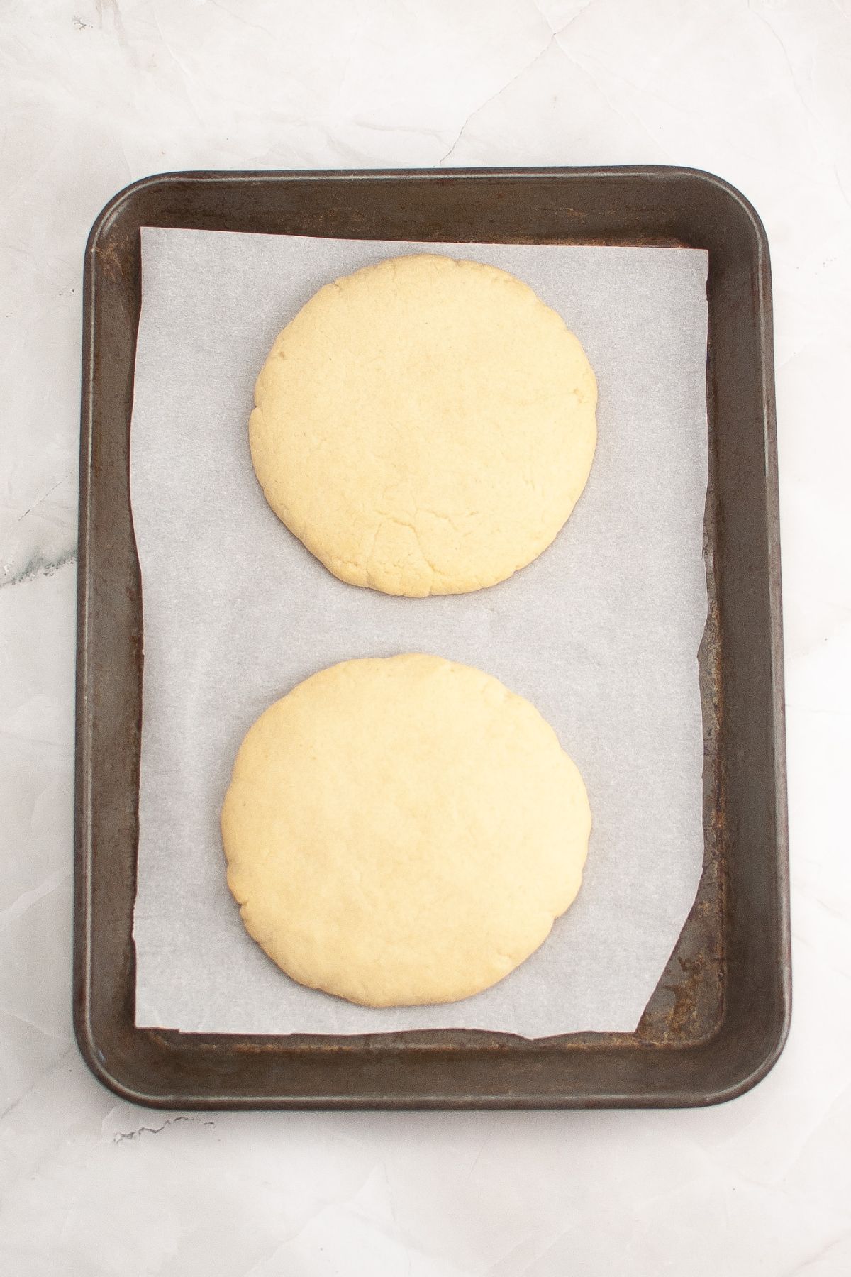 Two cookie dough balls on a parchment lined baking sheet ready for the oven.