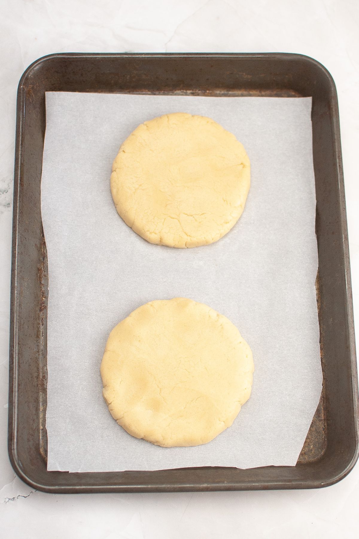 Cookie dough being spread out on a parchment lined baking sheet.