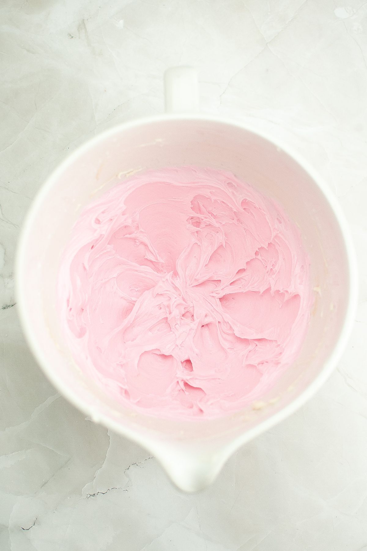 Pink frosting being mixed in a mixing bowl.