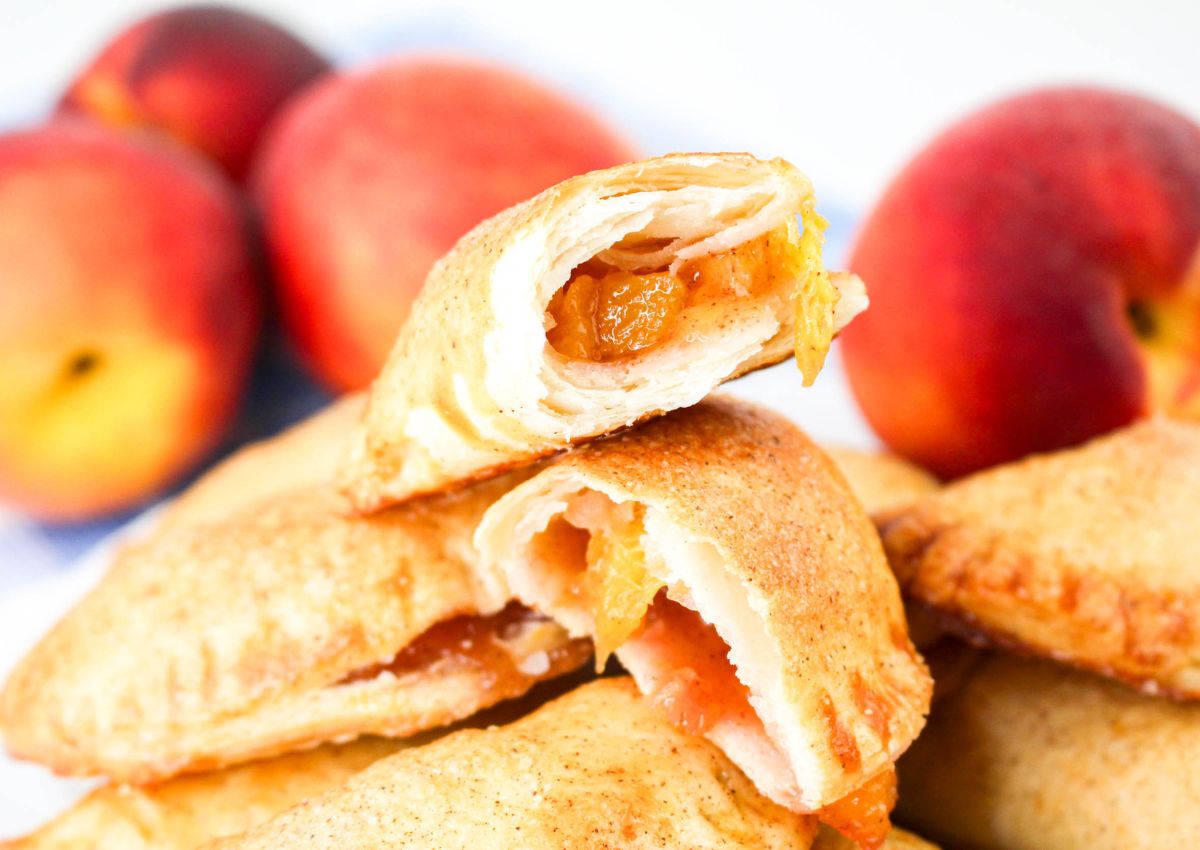 Peach hand pies stacked on a plate, with the top one broken in half.