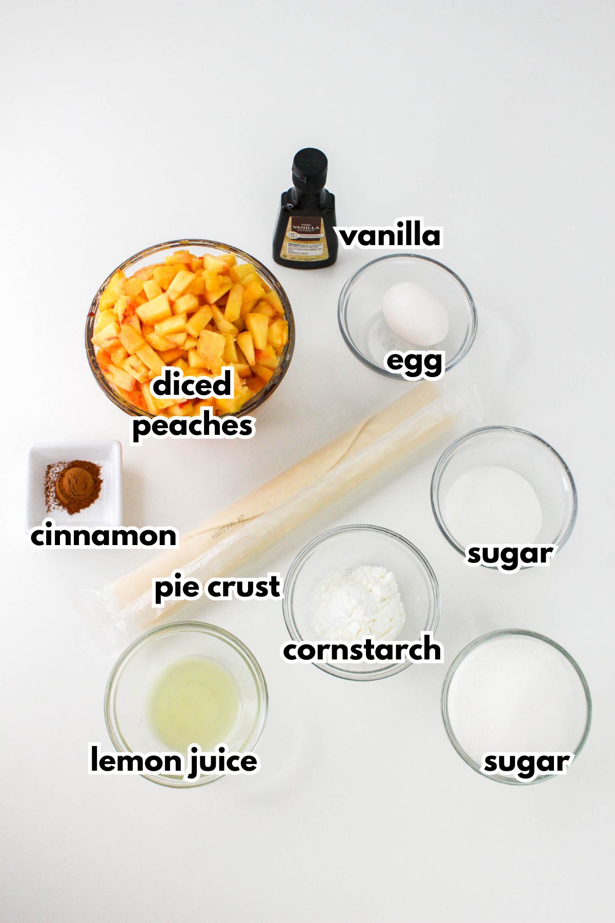 Bowls of diced peaches, vanilla extract, cinnamon, egg,sugar, cornstarch, lemon juice and a roll of pie crust on a counter.