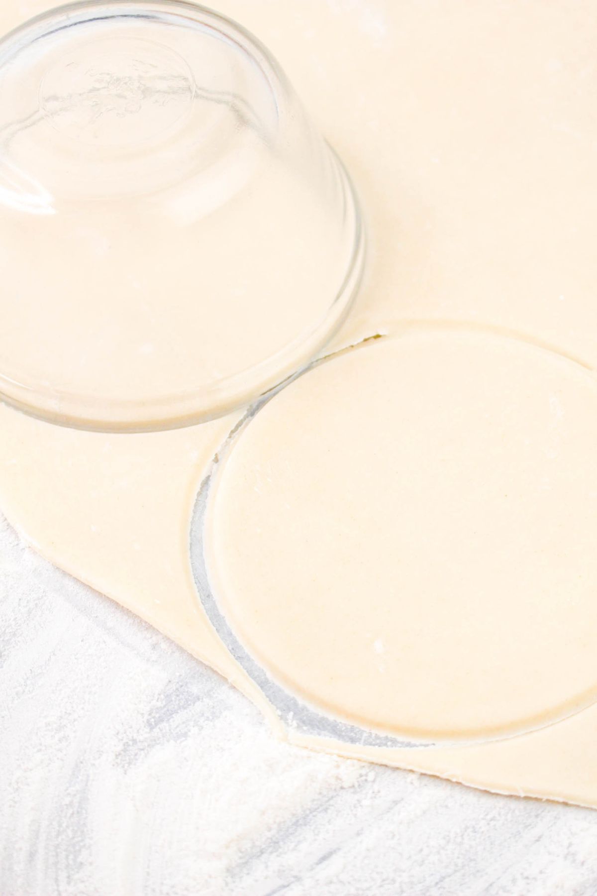 A glass bowl being used to cut circles out of dough.