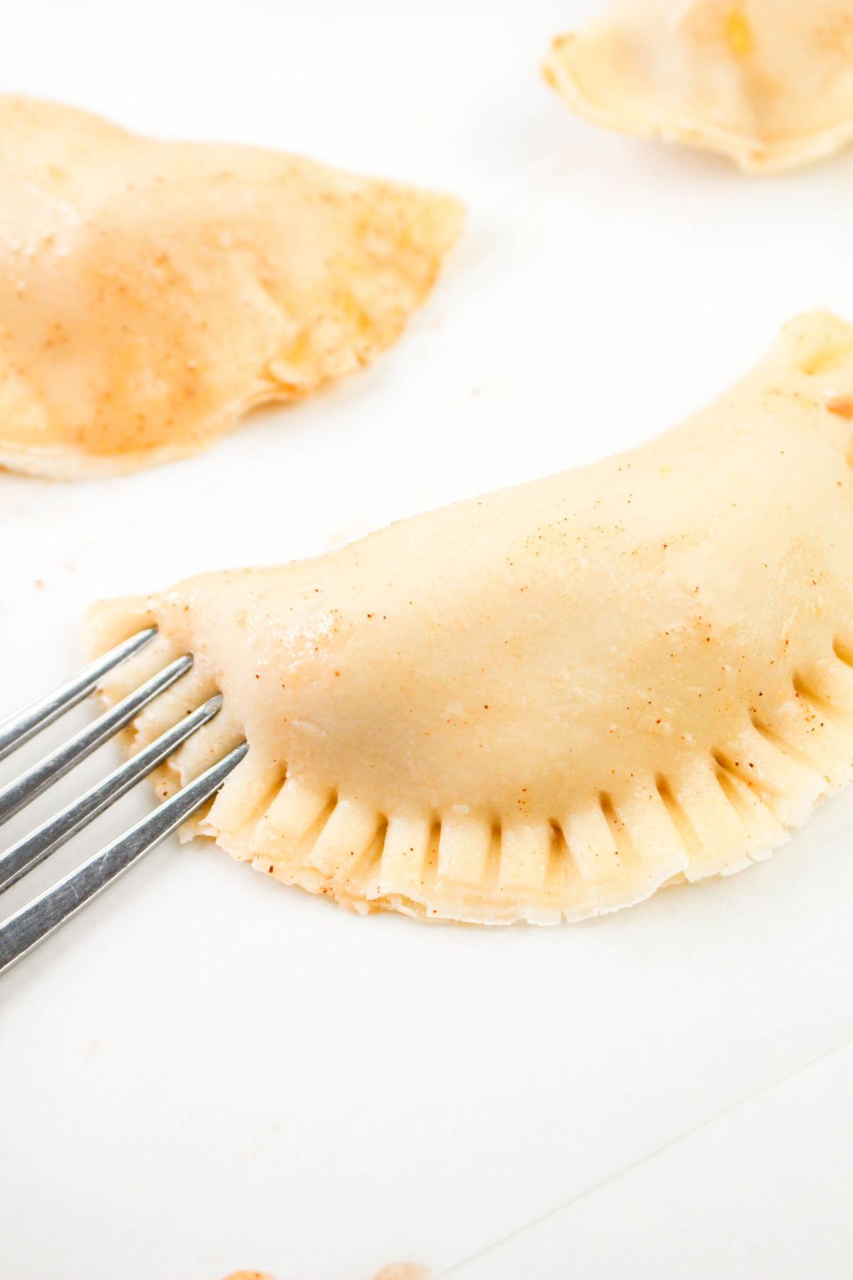 A fork being used to seal the edges of a crust on a parchment lined baking sheet.