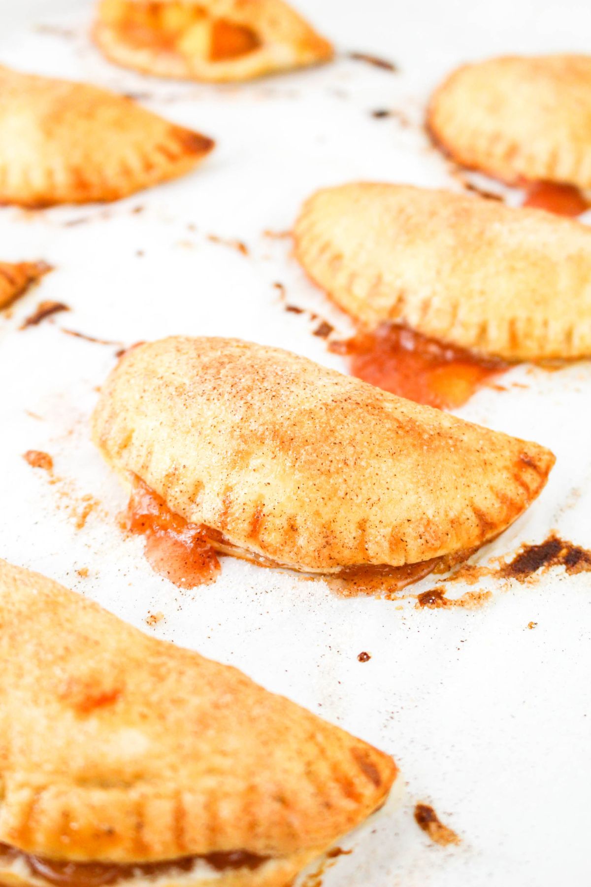 Peach hand pies baked on a parchment lined baking sheet cooling.