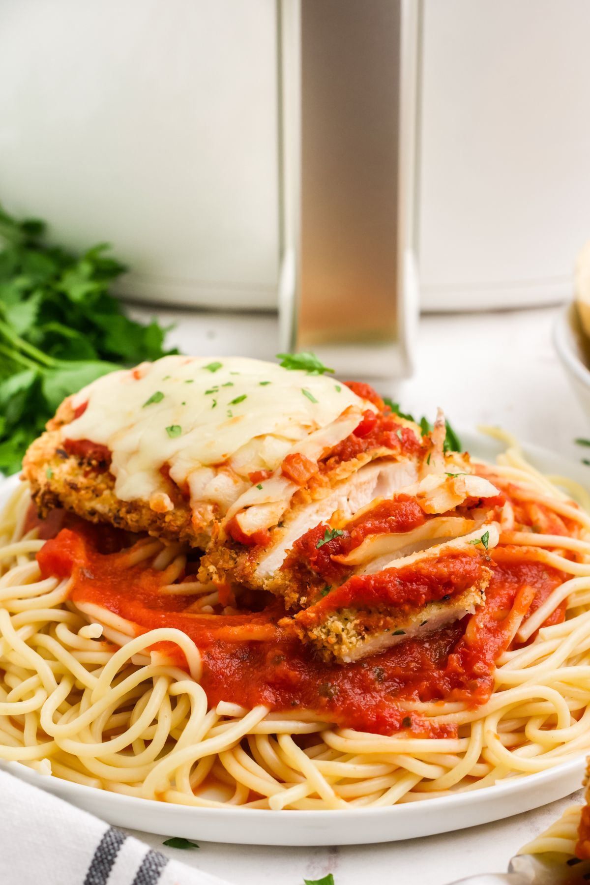 Plate of spaghetti topped with parmesan crusted chicken breast on a table ready to serve.