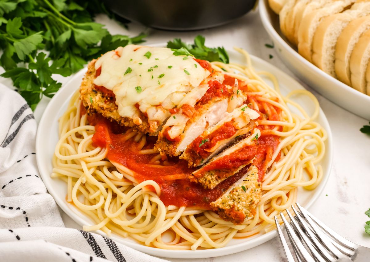 Plate of spaghetti topped with parmesan crusted chicken breast on a table ready to serve.