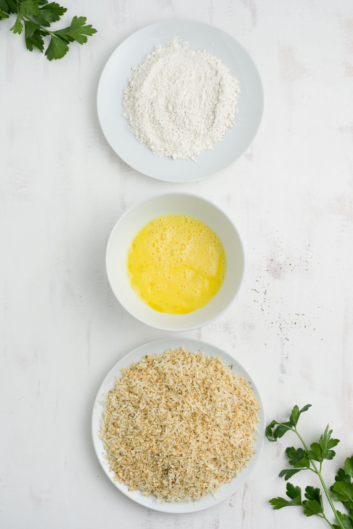 Bowls of flour, egg wash, and seasoned bread crumbs on a counter.