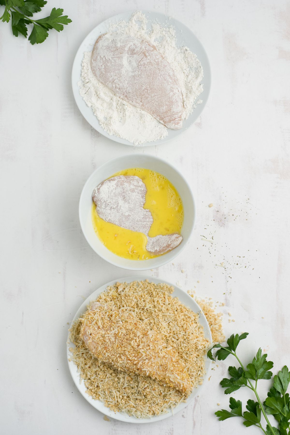 Chicken breasts being breaded in flour, egg wash, and seasonined bread crumbs.