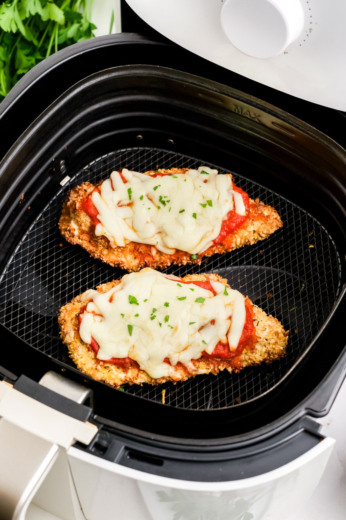 Two pieces of air fyrer parmesan crusted chicken breasts in the air fryer basket.