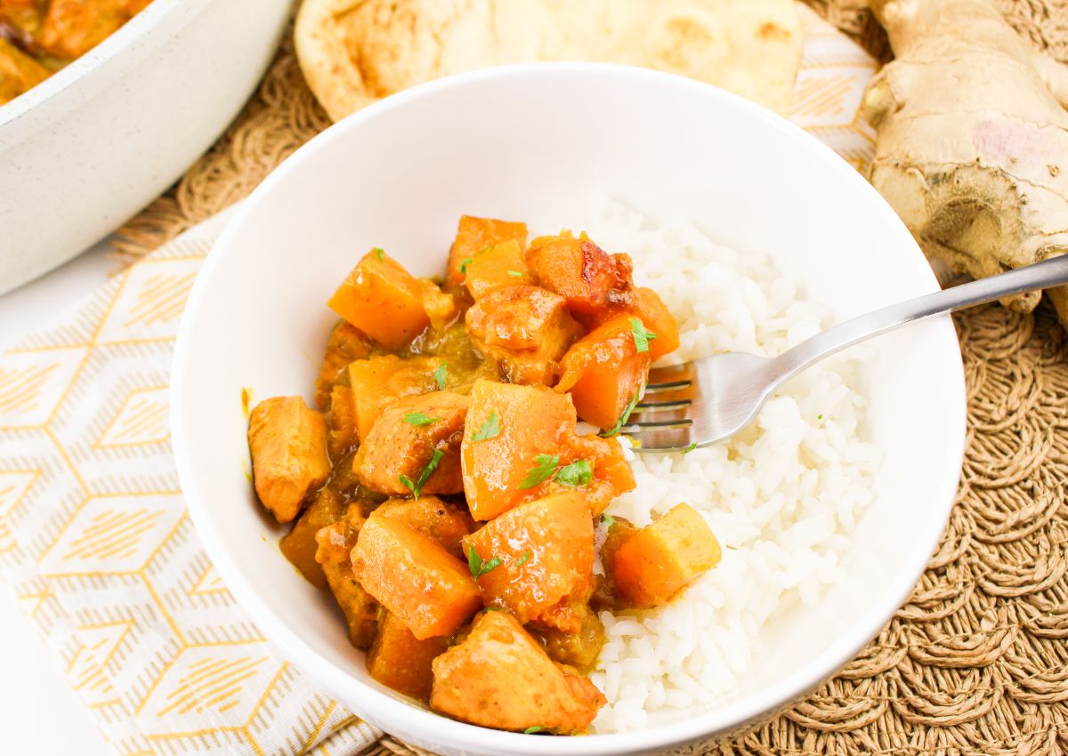 Bowl of pumpkin chicken curry served over a bed of white rice.